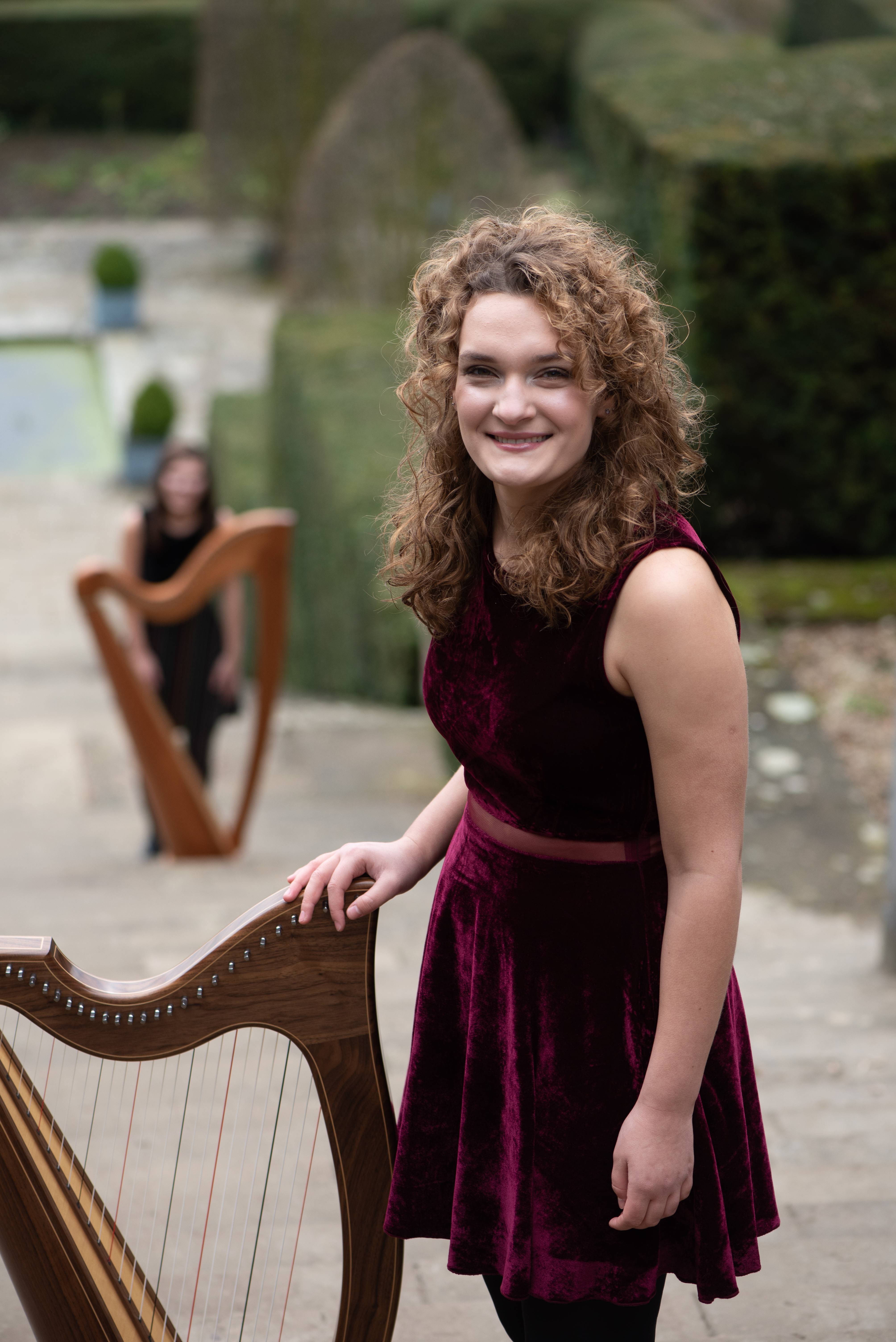 Karina, Harpist standing at the top of a staircase with Adel harpist in the background bl